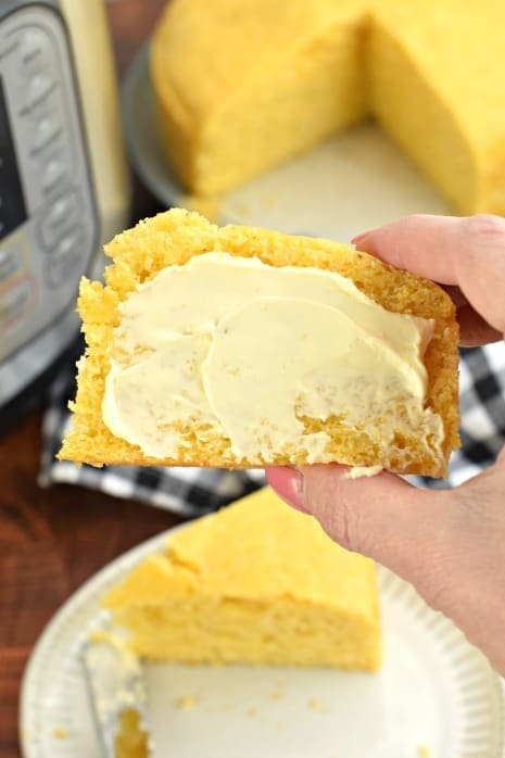 Hand holding a slice of cornbread cooked in Instant pot with butter spread. 