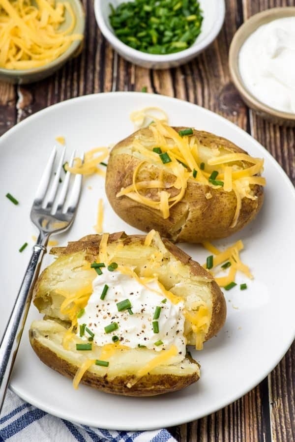 Baked potatoes with cream and grated cheese garnished with chopped onion leaves and pepper. 