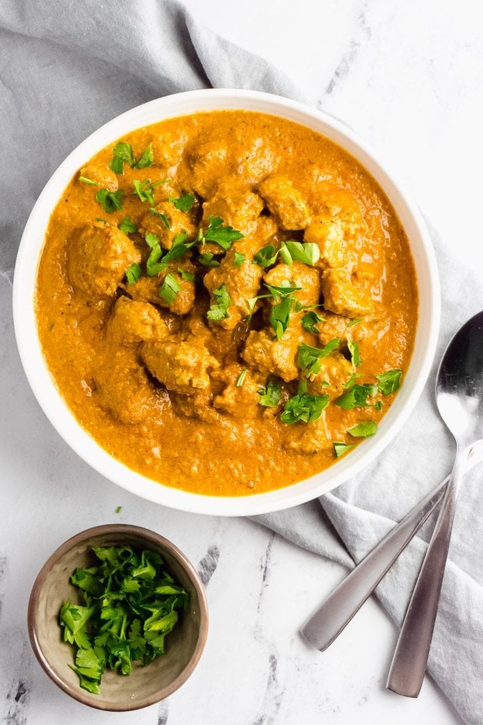 Butter chicken on a bowl garnished with chopped cilantro leaves. 