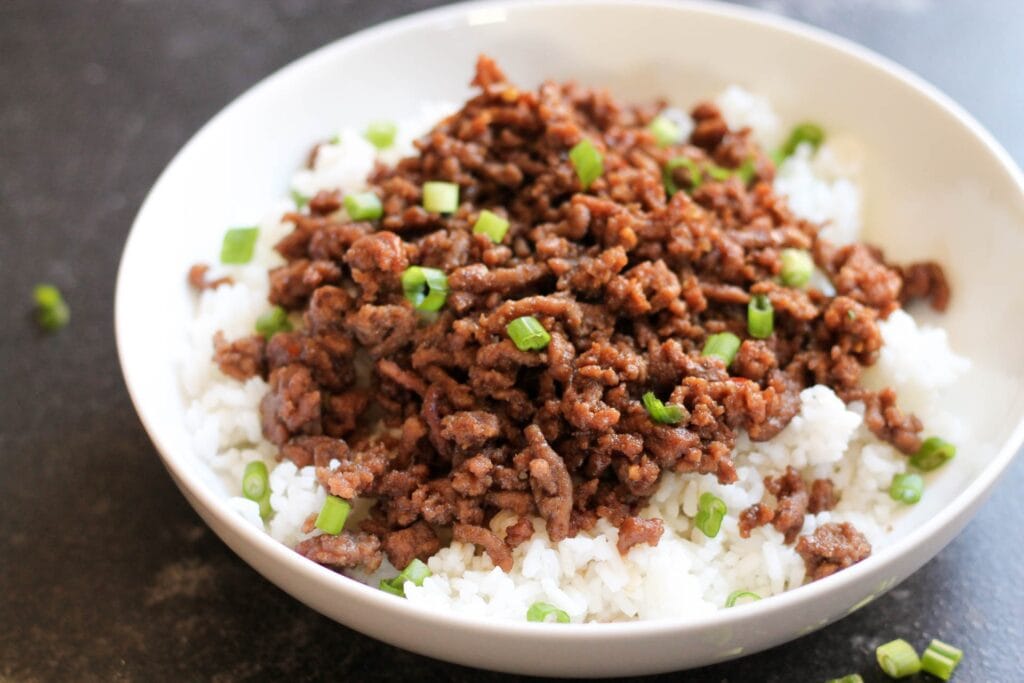 Rice topped with Korean beef dish served on a white bowl.