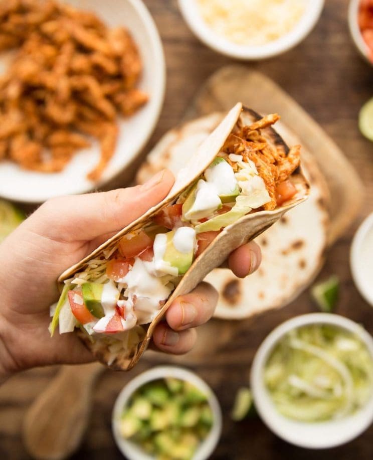 A person holding a taco made with leftover turkey meat with veggies on the side.