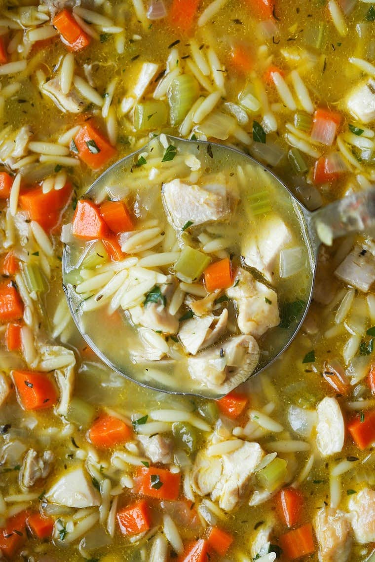 Chicken orzo soup loaded with chicken meat and veggies scooped with a steel ladle from a pot. 