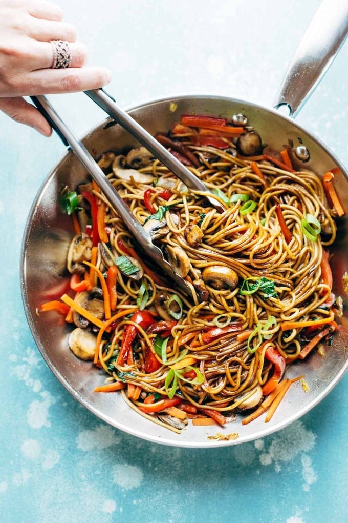 A person skillfully holds two chopsticks over a sizzling pan of delicious Lo Mein noodles