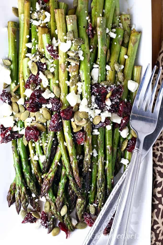 Asparagus with cranberries and feta cheese on a white plate. 