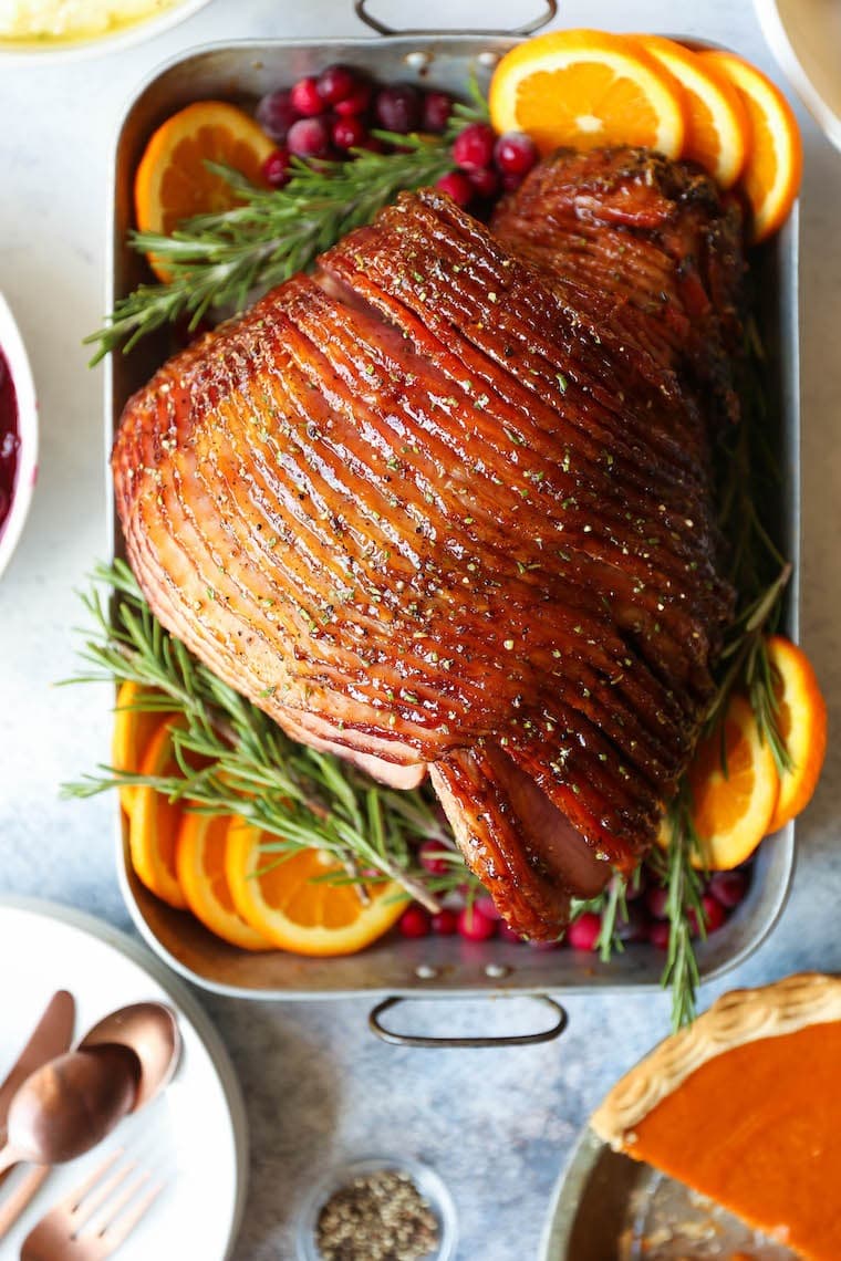 Sliced maple glazed ham on a roast pan with rosemary and sliced oranges. 