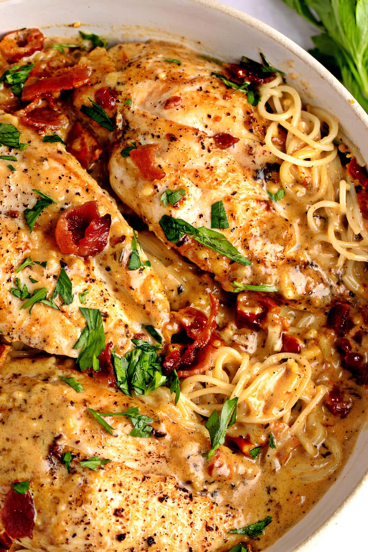 Creamy chicken breast cooked with pasta and sauce garnished with fried bacon bits.