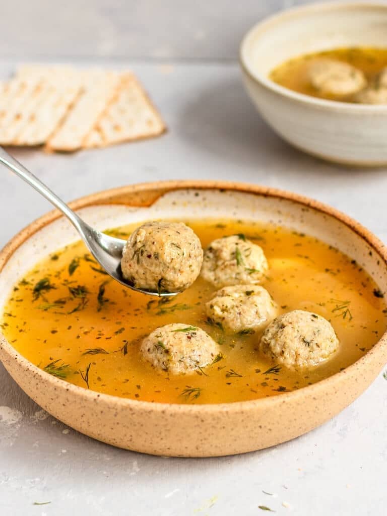 Spoon scooping meatballs on a bowl of homemade Matzo Ball Soup