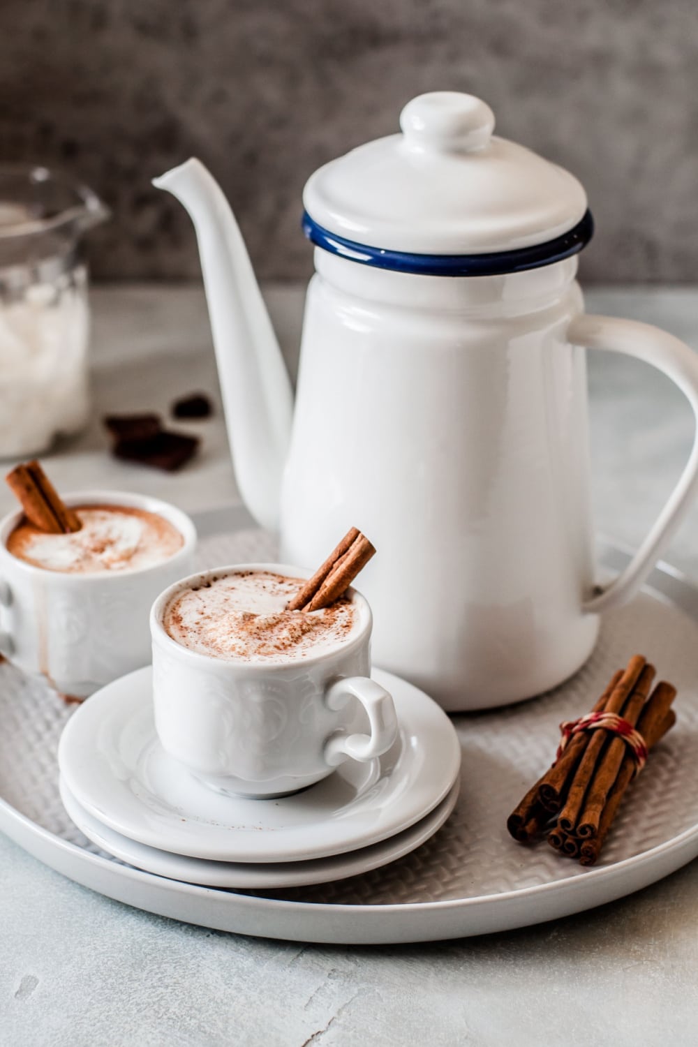 Mexican hot chocolate served in mugs with garnish of cream and cinnamon sticks on top. 