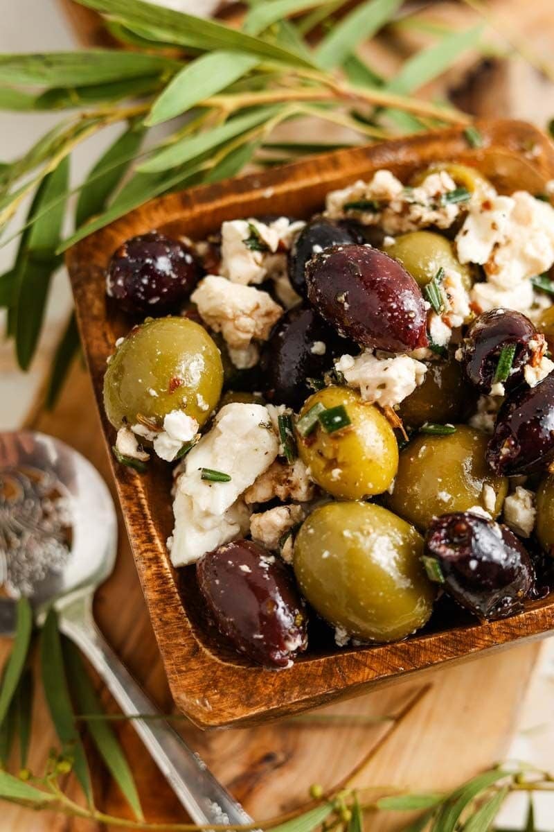 Marinated feta cheese and olives on a wooden bowl. 