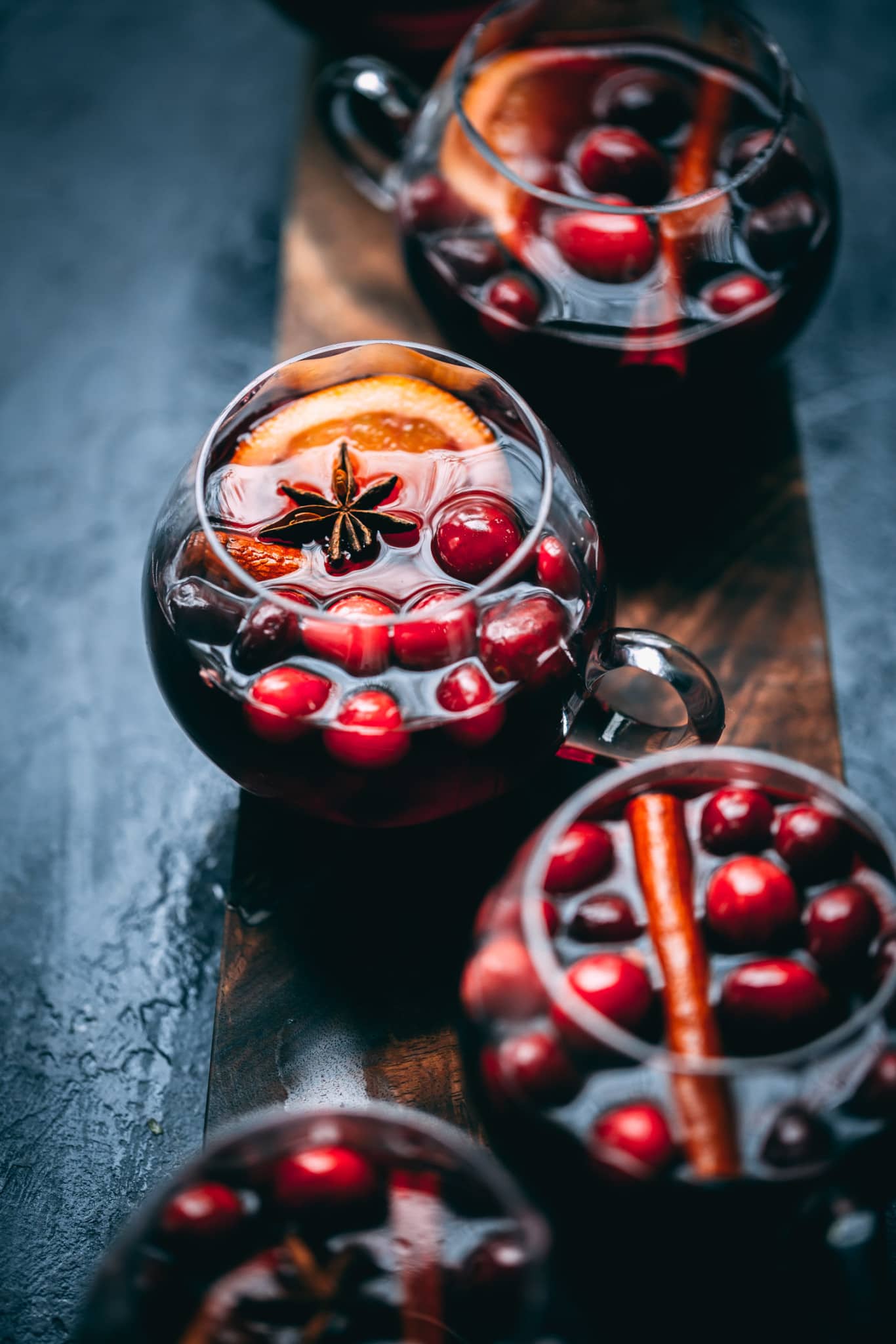 Glasses of Mulled wine garnished with fresh cranberries, cinnamon sticks and lemon slices.