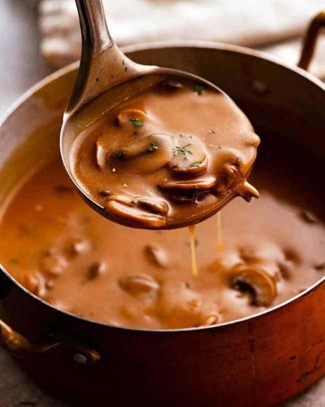 Ladle filled with a portion of mushroom gravy from a pot. 