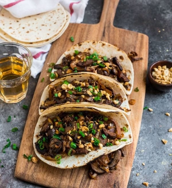 Mushroom tacos served on a wooden board garnished with chopped peanuts.