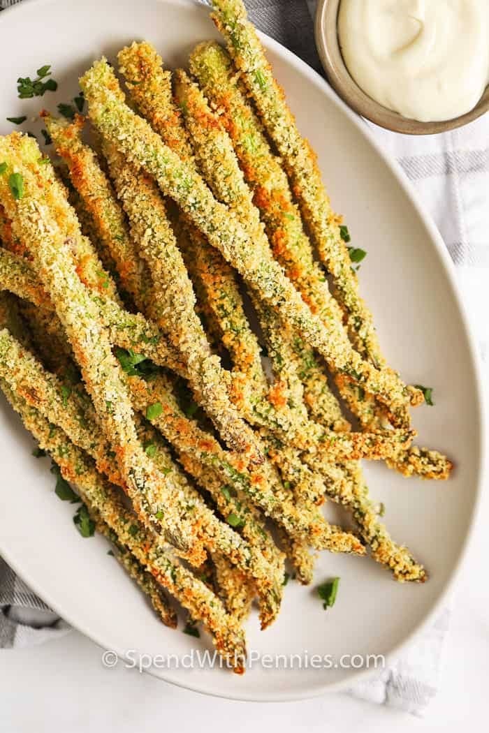 Breaded asparagus fries served on a white plate with white sauce dip on sides. 