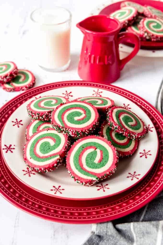 Pinwheel cookies coated with colorful sprinkles served on a Christmas themed red plate. 