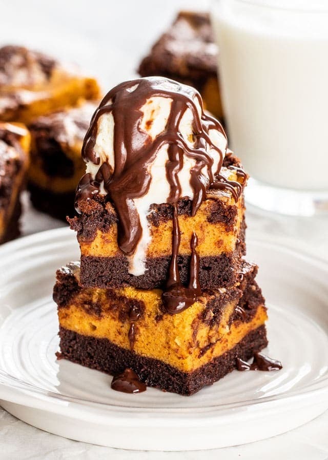 Homemade Pumpkin Cheesecake Brownies served on a plate with ice cream toppings and chocolate syrup