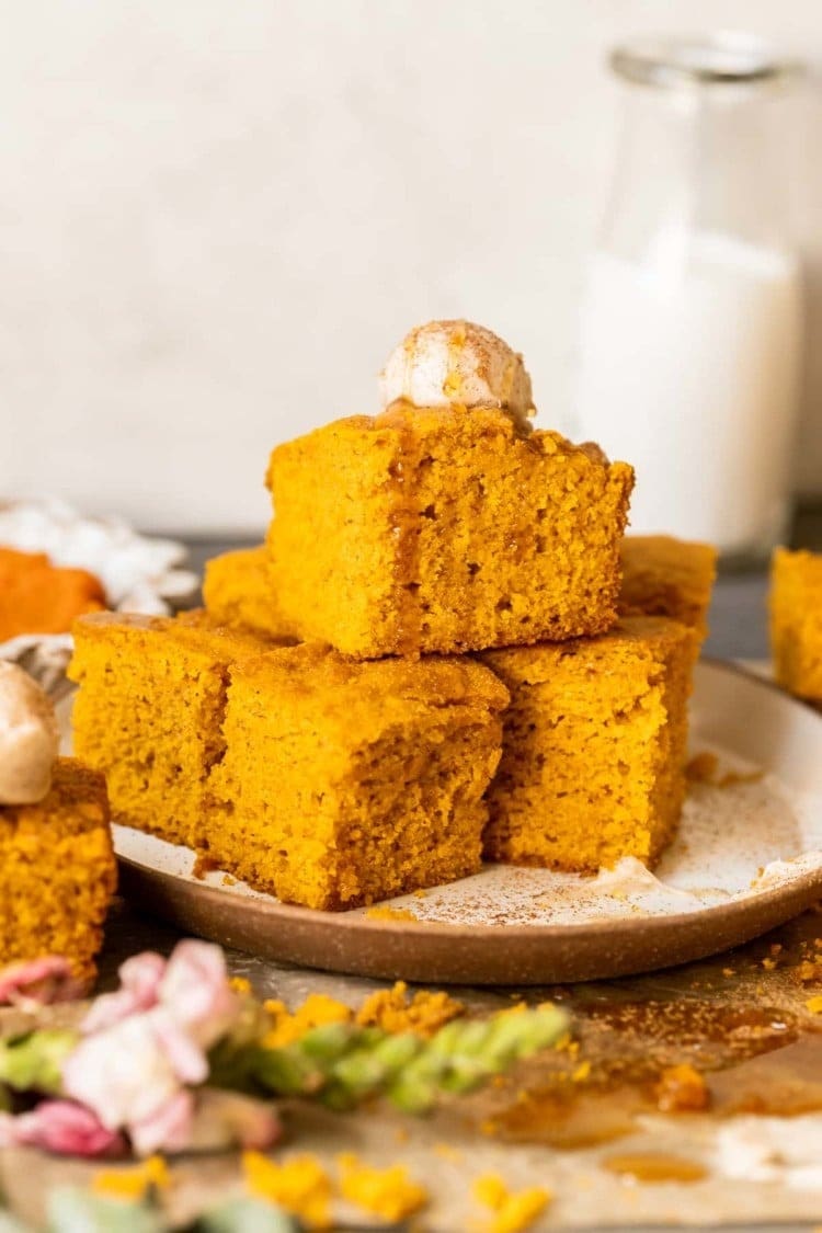 Slices of pumpkin cornbread stack on  a plate with vanilla on top. 
