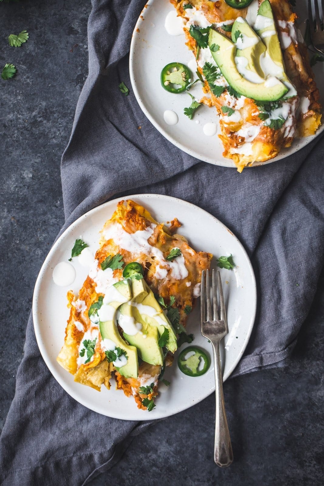 Spicy black bean chicken enchiladas with pumpkin sour cream sauce and sliced avocado on a plate. 