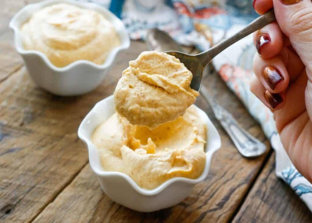 Spoon scooping pumpkin mousse in a small mug. 