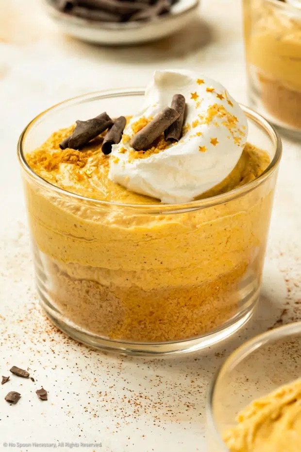 A glass of pumpkin mousse topped with whipped cream, cinnamon stick and spices. 