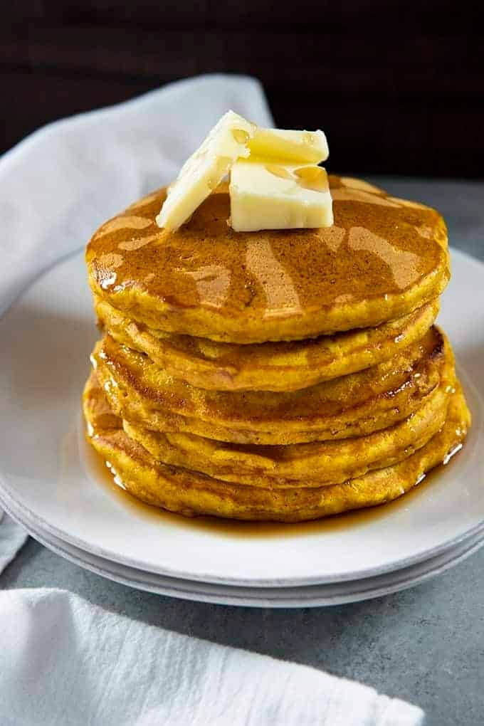 Stack of pumpkin pancakes dripping with syrup topped with slices of butter. 
