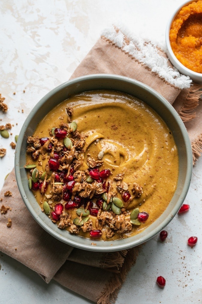 Pumpkin smoothie in a bowl  garnished with nuts and pomegranate arils and seeds. 