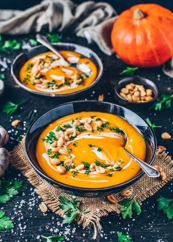 Pumpkin soup served on black bowls garnished with pumpkin seeds and cream.