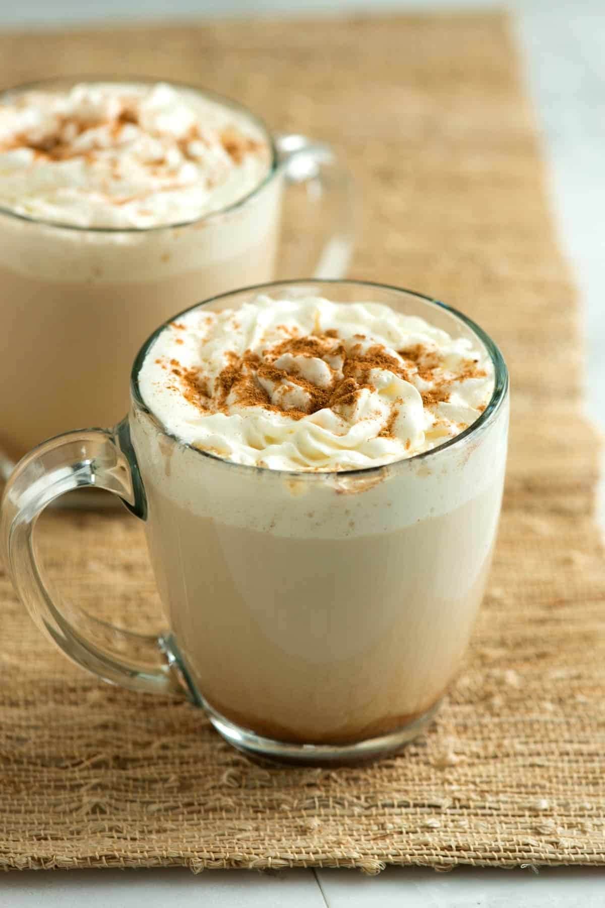 Glass of pumpkin spice latte with whipped cream and cinnamon powder on top. 