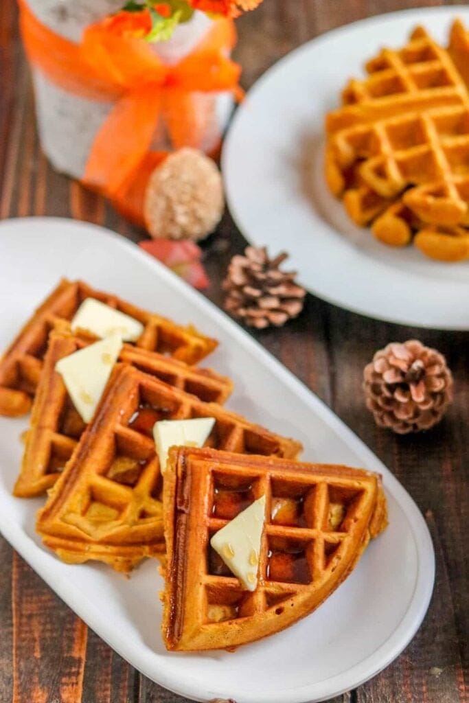 Homemade pumpkin spice waffles topped with butter slices and syrup. 