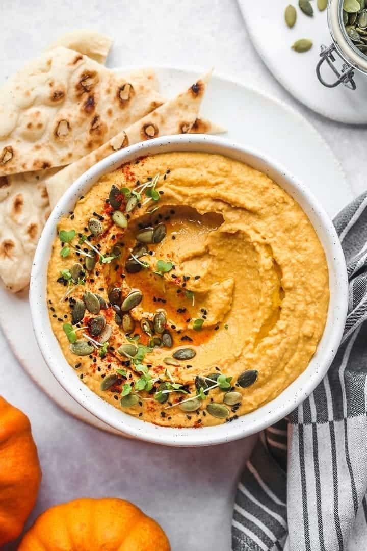Bowl of pumpkin hummus with seeds and herbs garnished. 