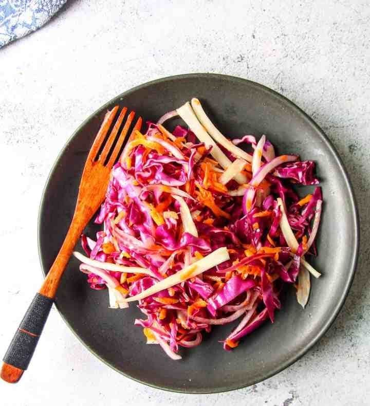 Red cabbage and fennel coleslaw served on a black plate with a wooden fork. 