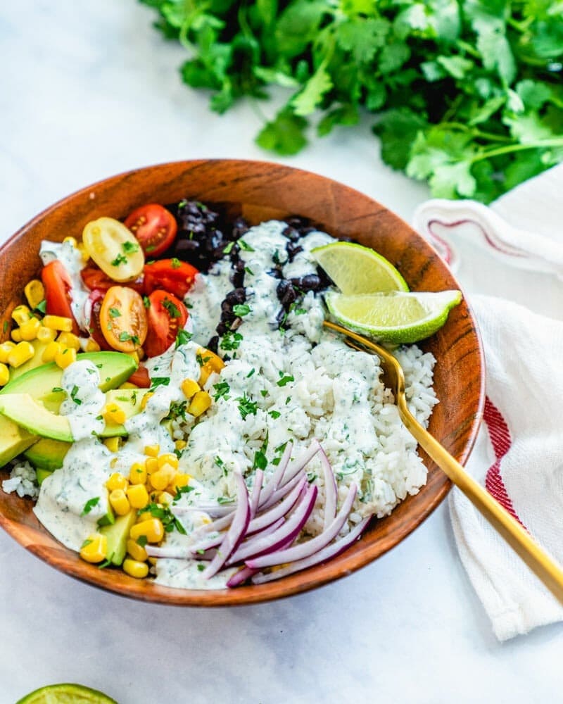 Rice in a wooden bowl with beans, tomatoes, avocado, and corn.
