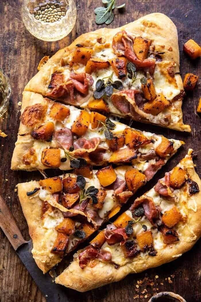 Butternut squash pizza sliced on top of a wooden surface. 