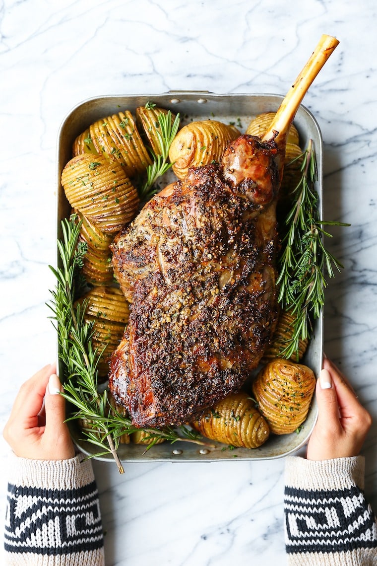 Roasted leg lamb seasoned with sliced potatoes and rosemary on a pan. 