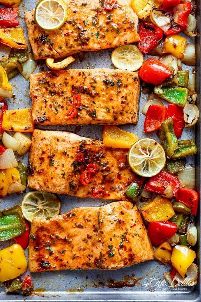 Salmon slices on sheet pan with onions and red, green, and yellow bell peppers. 