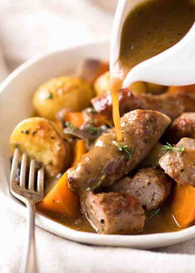 Gravy poured into baked sausage and vegetable served on a bowl. 