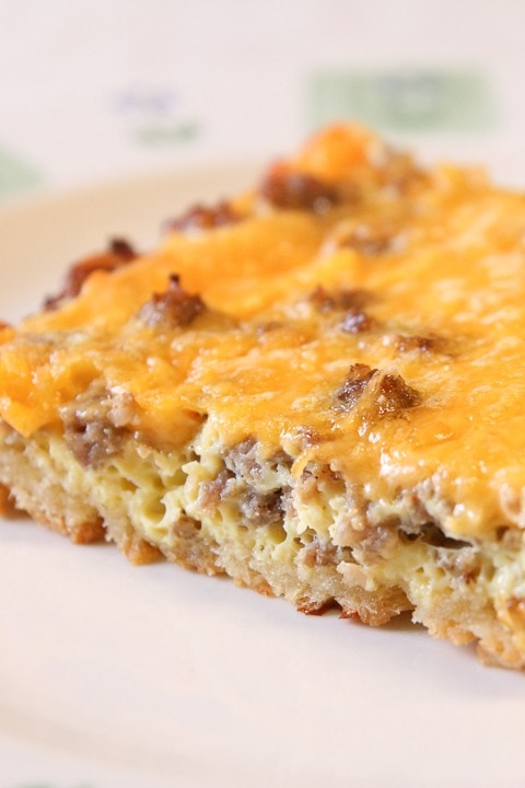 A slice serving of cheesy sausage breakfast casserole on a plate with eggs, cheese sausage and crescent roll dough. 