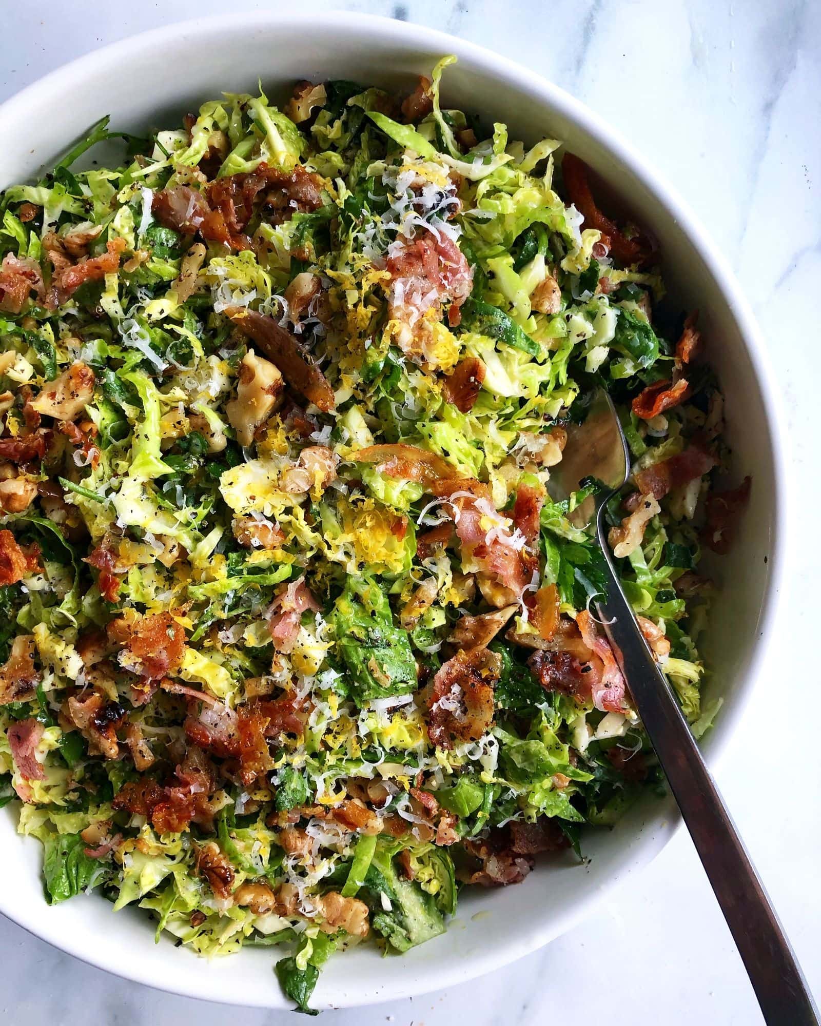 Shaved brussels sprout salad with crispy bacon, parmesan, and toasted walnuts on a bowl. 