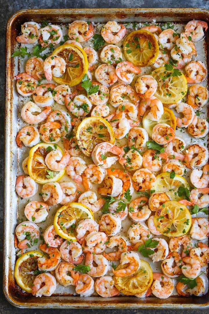 Buttered shrimp cooked with butter and lemon slices on a sheet pan seasoned and garnished with chopped parsley. 
