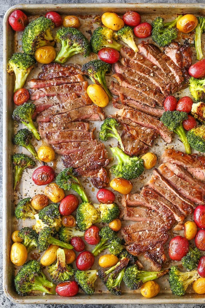 Sliced steak cooked on a sheet pan with broccoli, potatoes and cherry tomatoes. 