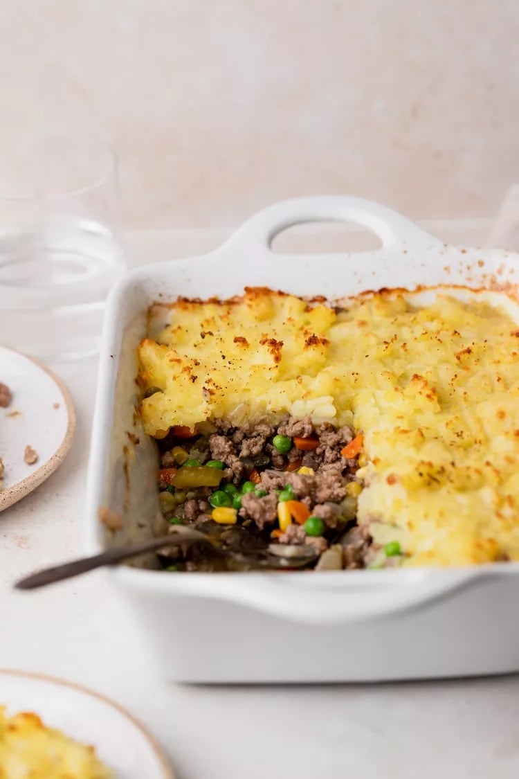 Shepherd’s Pie with ground beef, savory vegetables, topped with mashed potatoes filling on a white dish. 
