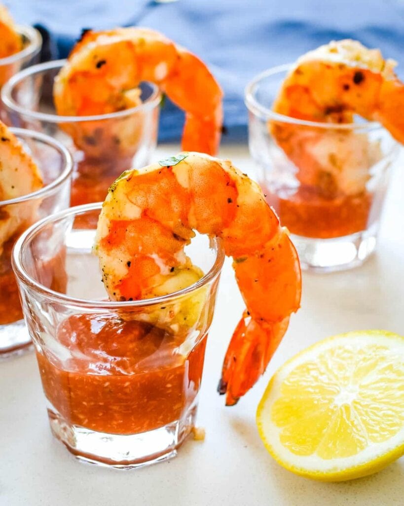Shrimp in shot glasses with sauce and lemon wedge on side. 