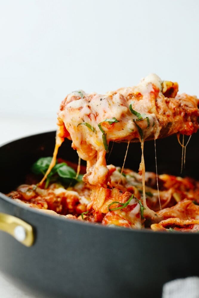 Wooden spoon scooping cheesy lasagna from a skillet. 