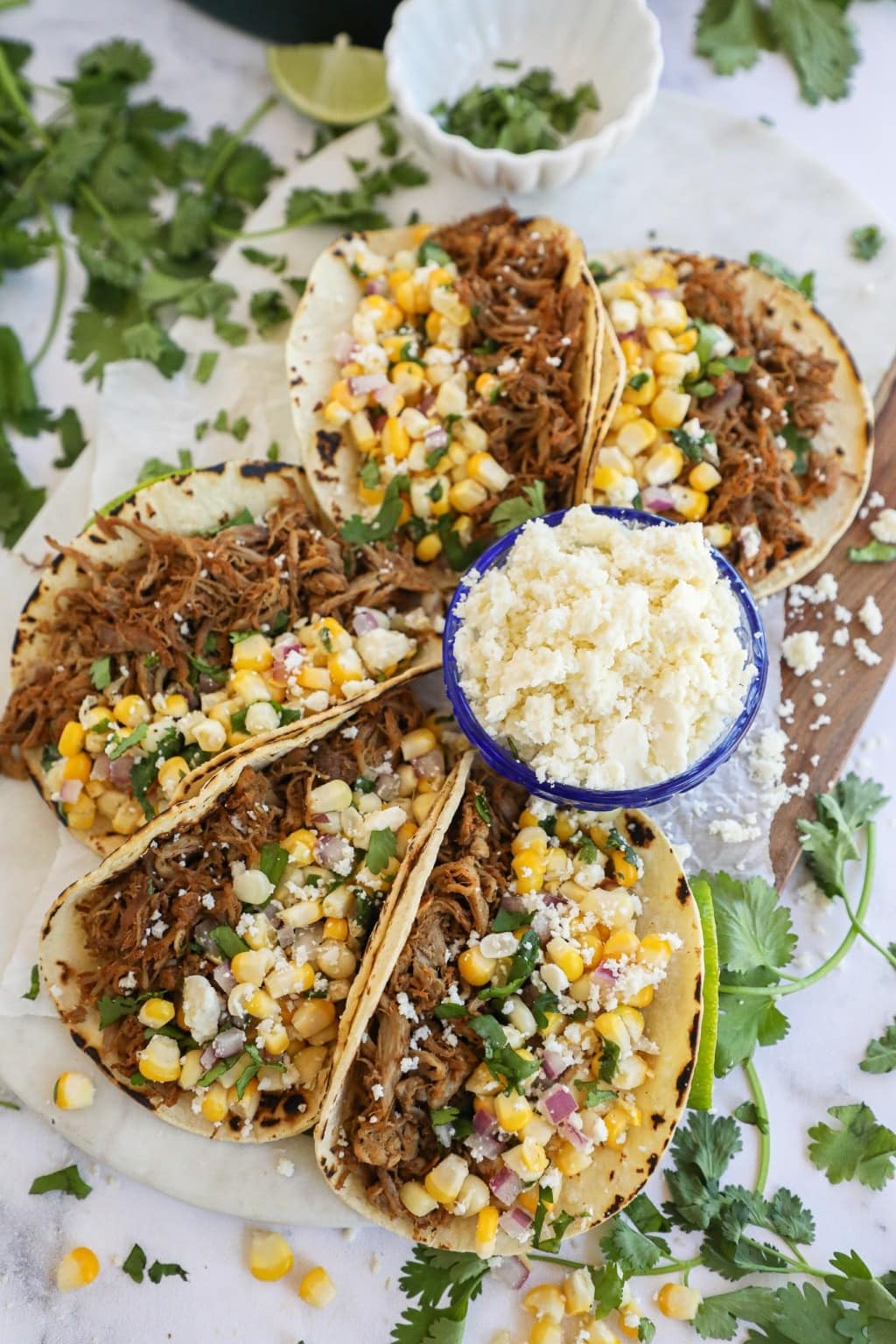 Slow Cooker Pork Tacos with corn, cilantro and a bowl of Cotija cheese