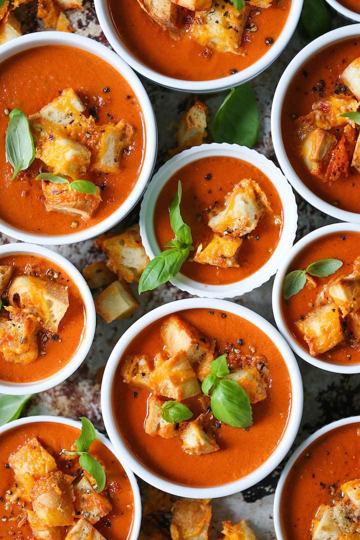 Tomato basil soup served in bowls topped with croutons and fresh basil leaves. 
