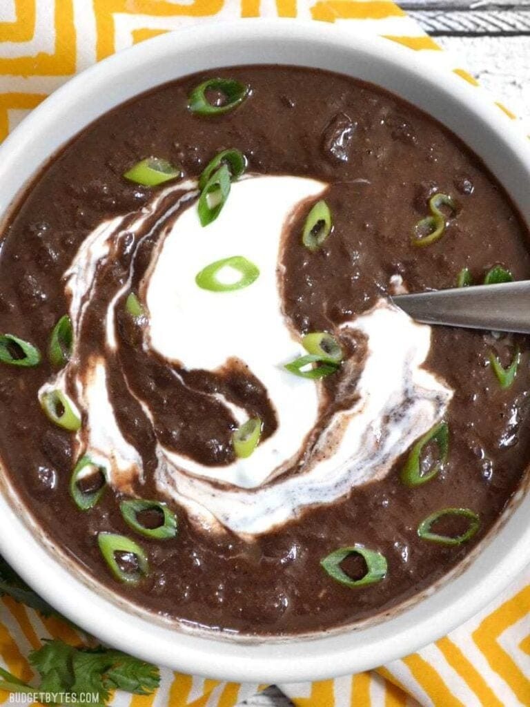 Black bean soup in a white bowl topped with sour cream. 