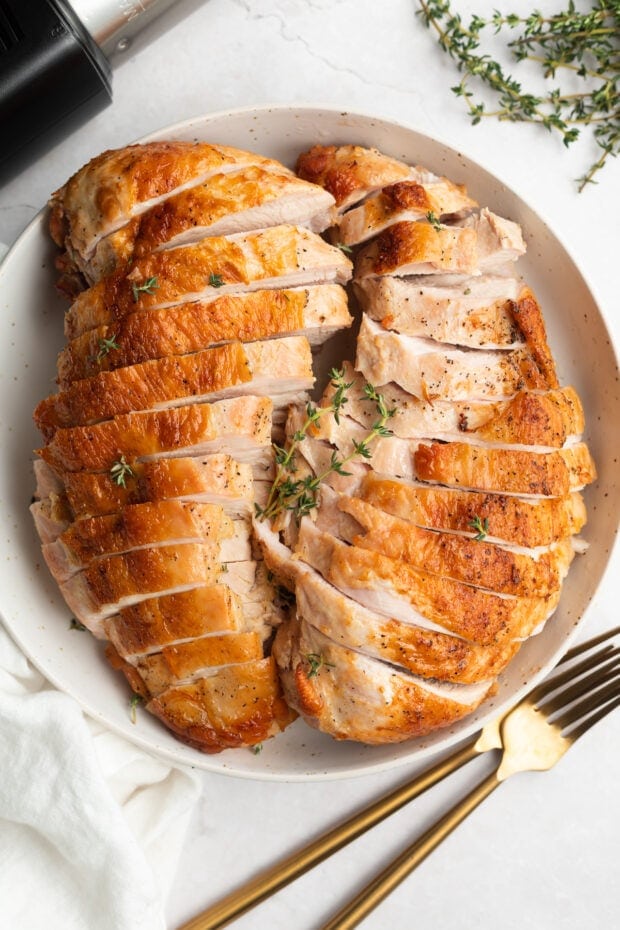 Sous Vide Turkey Breast with Crispy Skin on a round plate with two gold fork on the side