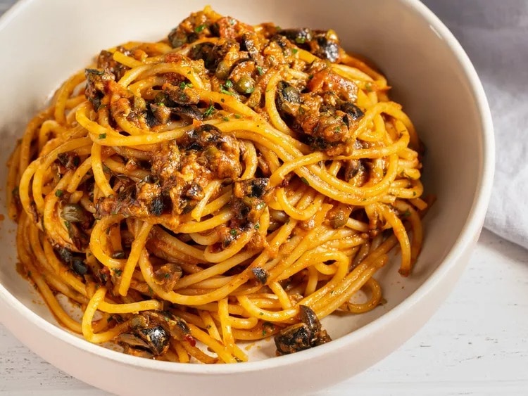 Spaghetti with meatballs, garlic and olives in a white bowl
