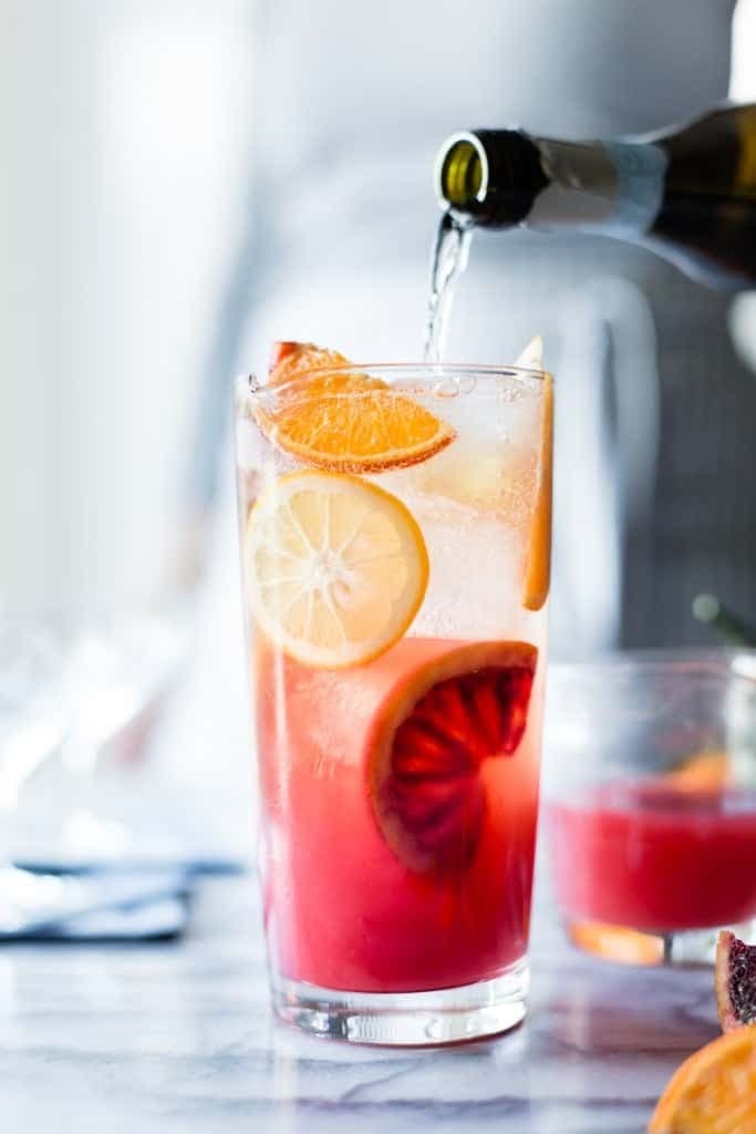 Wine pouring to a glass of sparkling citrus, lillet and prosecco punch garnished with slices of grapefruit and lemon. 