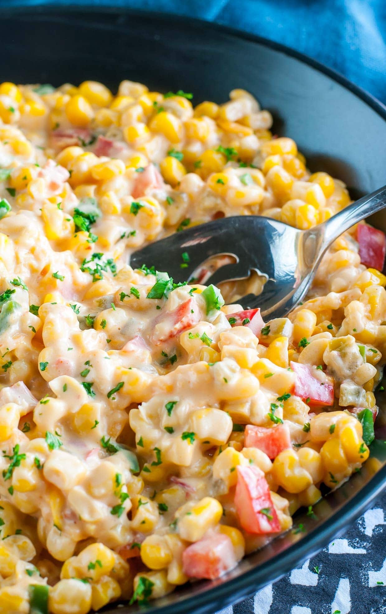 Creamy spicy southern hot corn in a black plate with a serving spoon.  