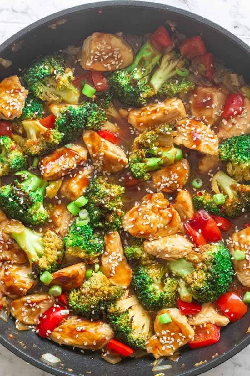 Chunks of breaded chicken, broccoli florets, and chopped bell peppers stir fry with sauce on a pan. 